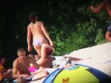 Señoras en topless rodeadas de hombres vestidos en la playa.