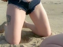 Rubia orina a través de sus pantalones cortos de mezclilla en la playa