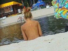 Rubia caliente se desnuda en la playa para nudistas