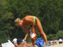 Teeny modelo rubia en topless en una playa nudista quitándose los pantalones
