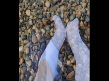 Jugando con mis pies en calcetines blancos con guijarros en la playa